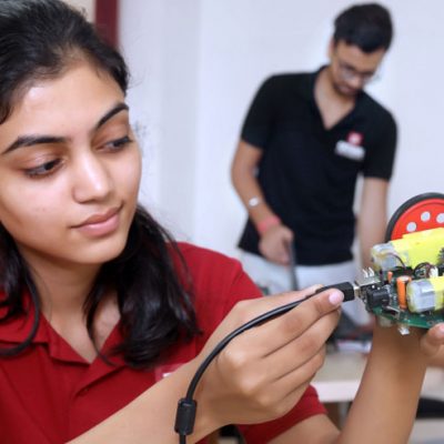 The image with a blurred background shows the students of chitkara university, one in black t-shirts and one in red, working on their projects.