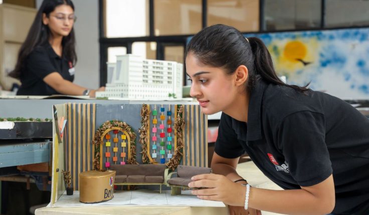 A female student arranging miniature sofas in her interior design model, practicing skills for a successful Career in Interior Design.