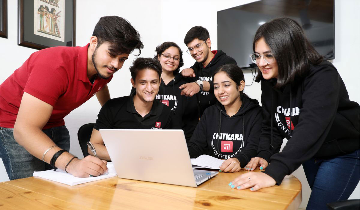 Students collaborating, with one student explaining strategies on a laptop, representing how an MBA is best for business growth through teamwork and leadership.