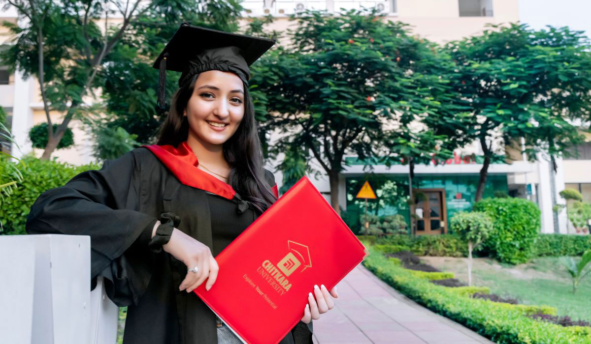 A female student smiling and proudly holding her MBA degree after completing a fully residential MBA program in India.